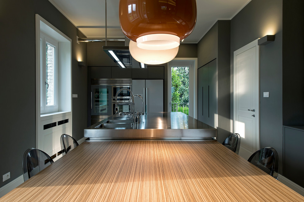 Geschlossene Moderne Küche mit integriertem Waschbecken, flächenbündigen Schrankfronten, Edelstahlfronten, Edelstahl-Arbeitsplatte, Küchengeräten aus Edelstahl, braunem Holzboden und Kücheninsel in Mailand