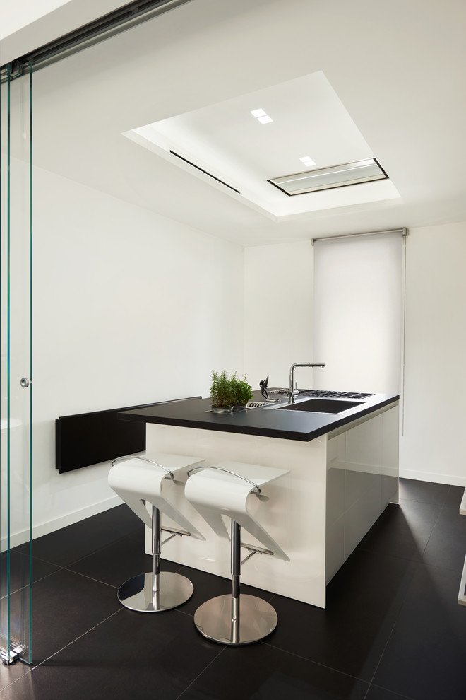 Cette image montre une cuisine minimaliste avec un évier 3 bacs, des portes de placard blanches, un plan de travail en quartz modifié, un électroménager en acier inoxydable, un sol en carrelage de porcelaine, îlot et un sol noir.
