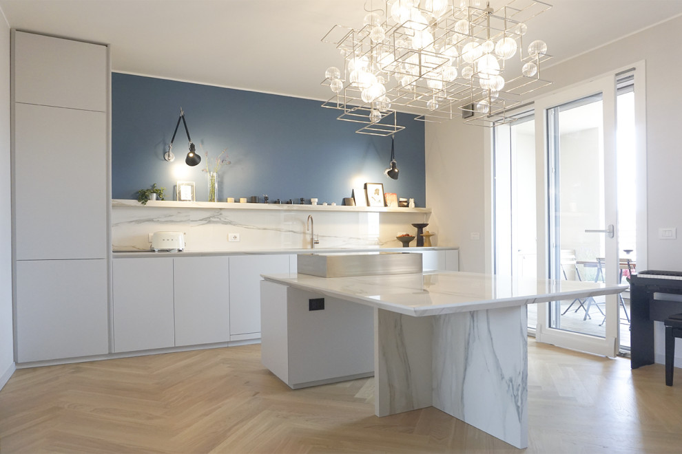 Example of a large trendy single-wall light wood floor and brown floor eat-in kitchen design in Milan with white cabinets, marble countertops, white backsplash, marble backsplash, stainless steel appliances, an island and white countertops