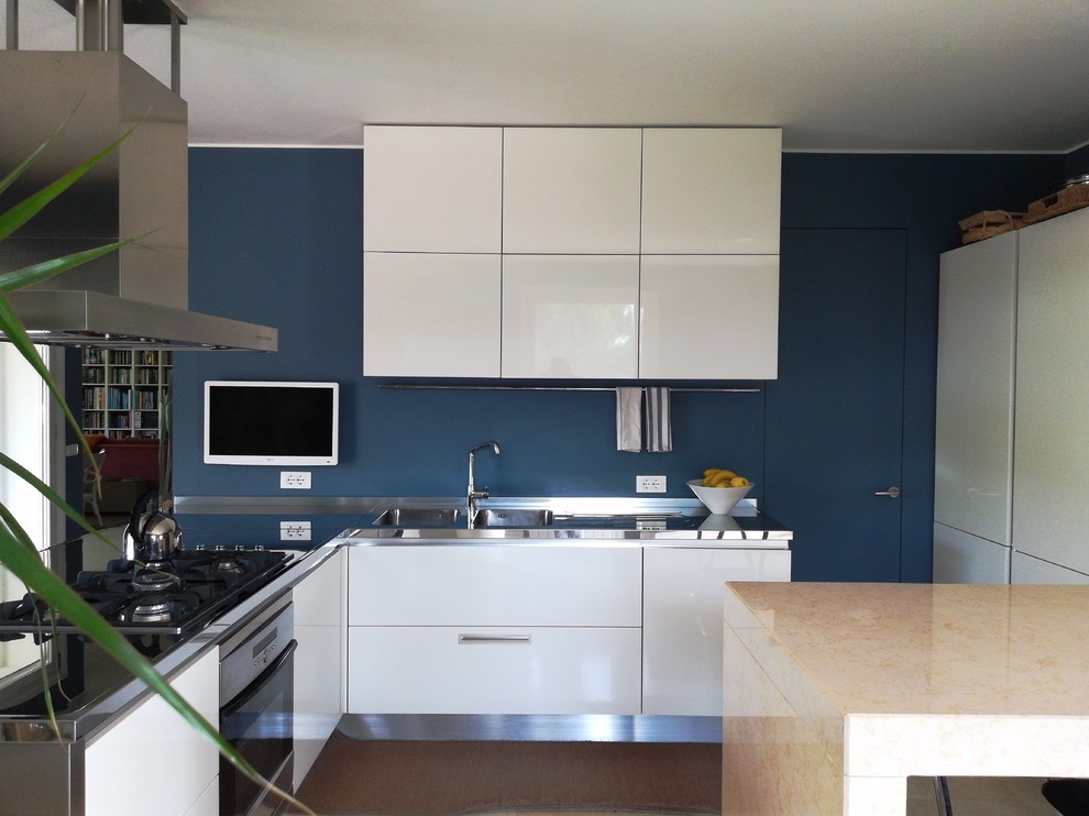 Large modern l-shaped open plan kitchen in Milan with a double-bowl sink, beaded cabinets, white cabinets, stainless steel worktops, glass sheet splashback, white appliances, marble flooring, no island and beige floors.
