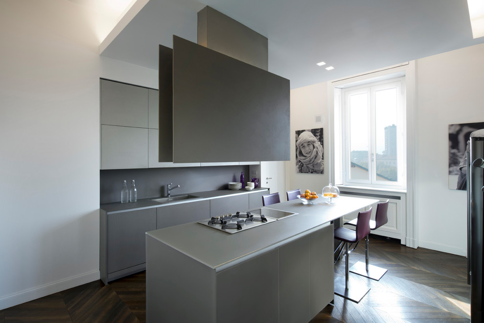 Cette image montre une cuisine américaine linéaire minimaliste de taille moyenne avec un placard à porte plane, des portes de placard grises, une crédence grise et îlot.