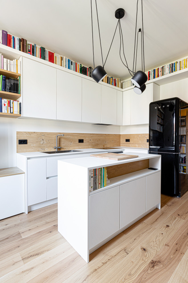 Photo of a medium sized scandinavian l-shaped kitchen/diner in Milan with a submerged sink, flat-panel cabinets, white cabinets, wood worktops, wood splashback, black appliances, light hardwood flooring, an island, white worktops and a drop ceiling.