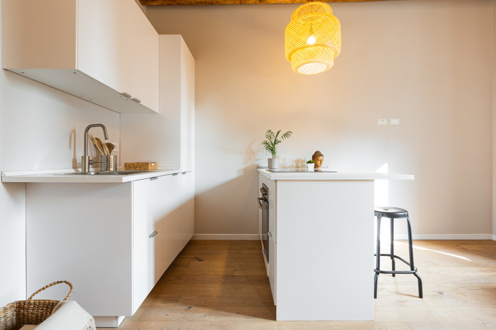 Inspiration för små skandinaviska linjära vitt kök med öppen planlösning, med en dubbel diskho, släta luckor, vita skåp, laminatbänkskiva, ljust trägolv och en köksö