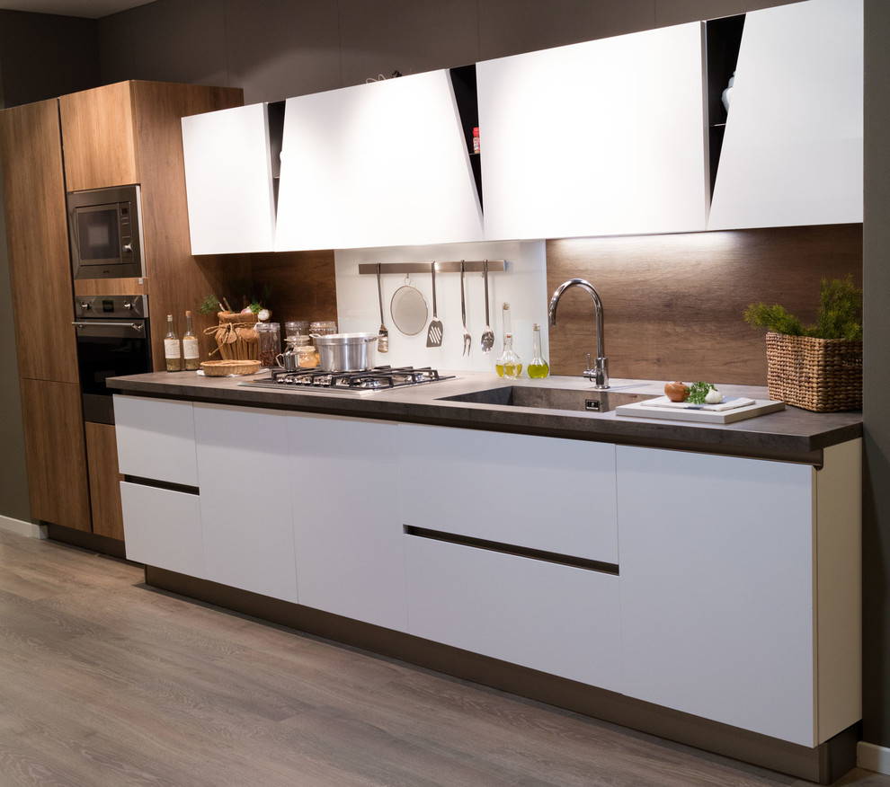 Bild på ett mellanstort funkis linjärt kök med öppen planlösning, med en integrerad diskho, släta luckor, vita skåp, glaspanel som stänkskydd, rostfria vitvaror, mellanmörkt trägolv och brunt stänkskydd