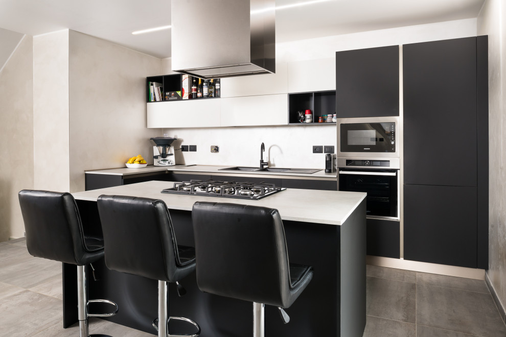 Photo of a medium sized modern l-shaped kitchen/diner in Turin with a double-bowl sink, flat-panel cabinets, black cabinets, laminate countertops, white splashback, porcelain splashback, stainless steel appliances, porcelain flooring, an island, grey floors and white worktops.