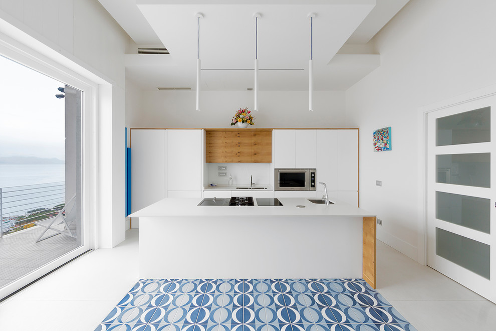 Cette image montre une cuisine parallèle design avec un évier encastré, un placard à porte plane, des portes de placard blanches, un électroménager noir, îlot, un sol multicolore et un plan de travail blanc.