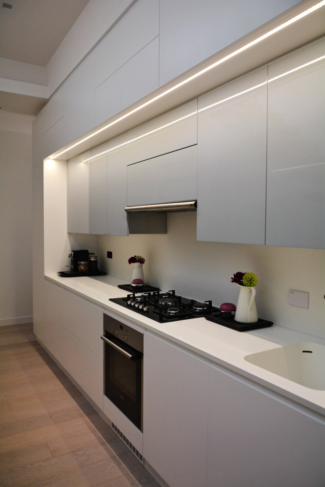 Immagine di una piccola cucina design con lavello integrato, ante lisce, ante bianche, top in superficie solida, elettrodomestici neri e pavimento in legno massello medio