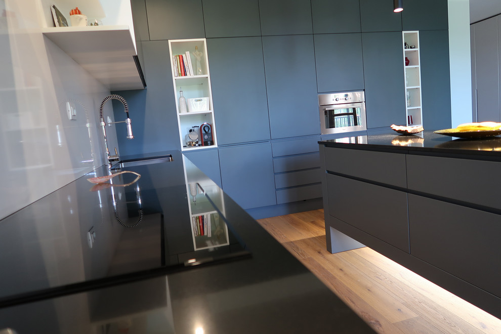 Diseño de cocina contemporánea grande con fregadero integrado, electrodomésticos negros, suelo de madera clara, una isla y encimeras negras
