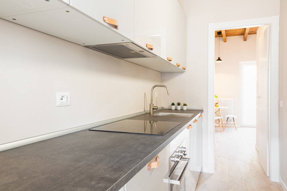 Small scandinavian single-wall enclosed kitchen in Milan with a single-bowl sink, flat-panel cabinets, white cabinets, white splashback, light hardwood flooring, no island, black worktops and exposed beams.