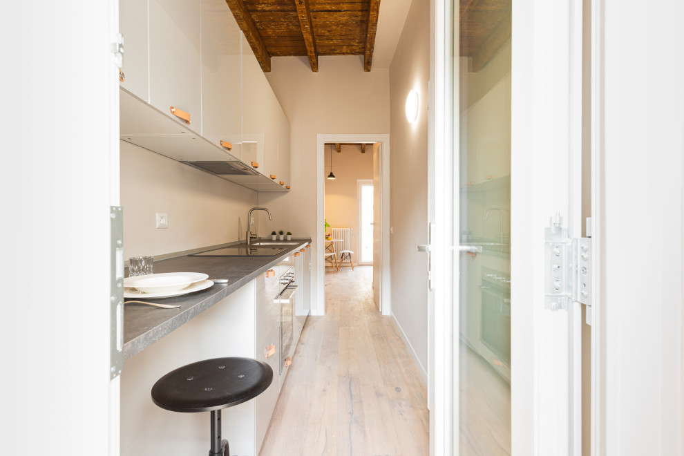 Design ideas for a small scandi single-wall enclosed kitchen in Milan with a single-bowl sink, flat-panel cabinets, white cabinets, white splashback, light hardwood flooring, no island, black worktops and exposed beams.