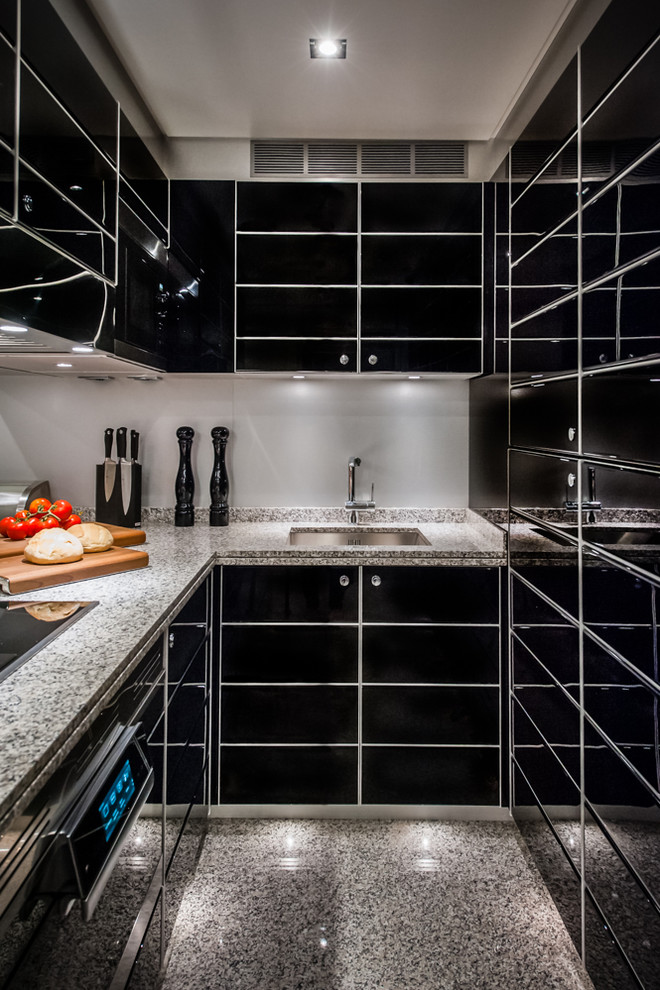 Bild på ett mellanstort, avskilt funkis u-kök, med en undermonterad diskho, släta luckor, svarta skåp, granitbänkskiva, grått stänkskydd, svarta vitvaror och grått golv