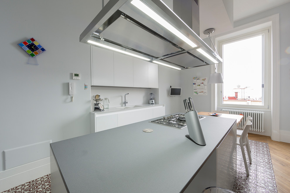Idéer för ett modernt grå kök, med en integrerad diskho, släta luckor, vita skåp, vitt stänkskydd, glaspanel som stänkskydd, rostfria vitvaror, klinkergolv i keramik, en köksö och flerfärgat golv