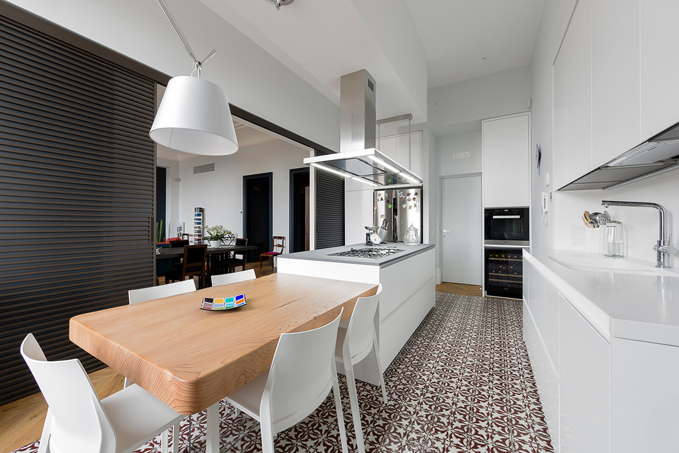 Moderne Küche mit integriertem Waschbecken, flächenbündigen Schrankfronten, weißen Schränken, Küchenrückwand in Weiß, Glasrückwand, Küchengeräten aus Edelstahl, Keramikboden, Kücheninsel, buntem Boden und grauer Arbeitsplatte in Neapel