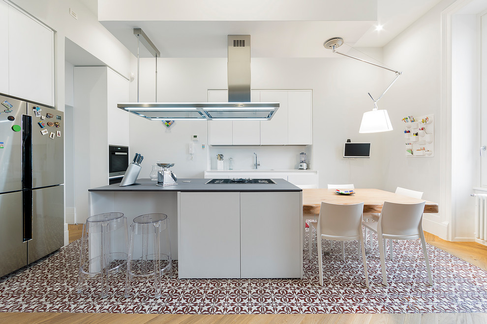 Idéer för ett modernt grå kök och matrum, med släta luckor, vita skåp, vitt stänkskydd, glaspanel som stänkskydd, rostfria vitvaror, klinkergolv i keramik, en köksö och flerfärgat golv
