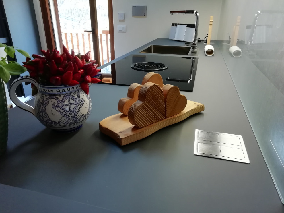 Modelo de cocina comedor minimalista sin isla con armarios con paneles lisos, puertas de armario grises, salpicadero de vidrio templado y encimeras grises