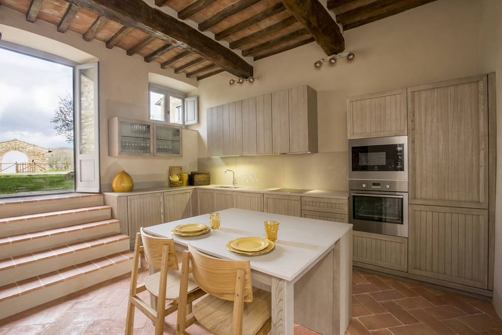 Mediterrane Wohnküche in L-Form mit Unterbauwaschbecken, Schrankfronten mit vertiefter Füllung, hellen Holzschränken, Küchengeräten aus Edelstahl, Terrakottaboden, Kücheninsel und Küchenrückwand in Beige in Florenz