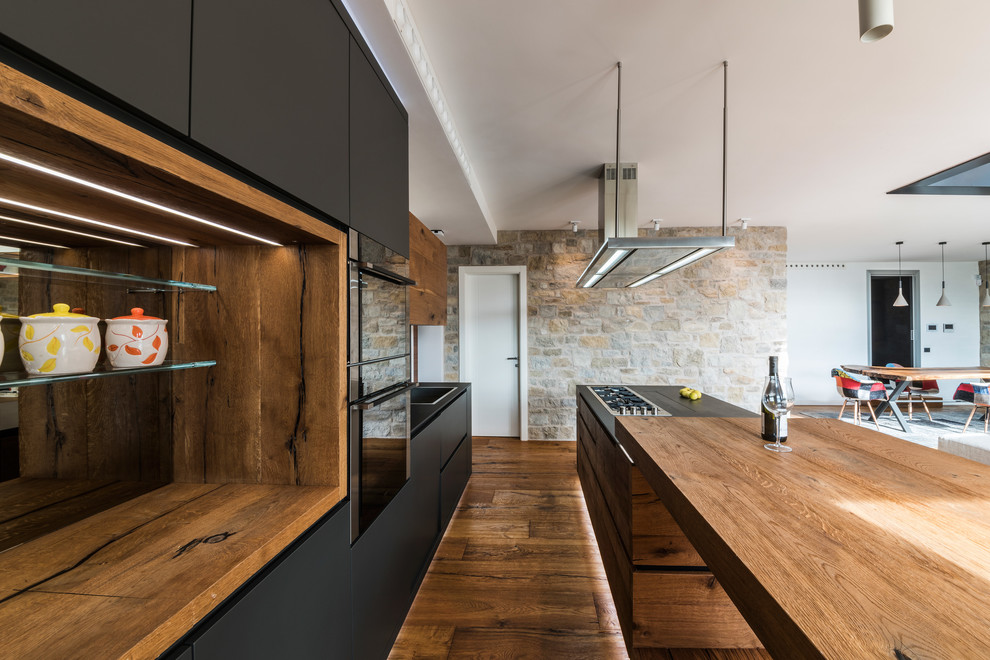Идея дизайна: кухня-гостиная в стиле кантри с накладной мойкой, черными фасадами, деревянной столешницей, черным фартуком, фартуком из сланца, паркетным полом среднего тона и островом