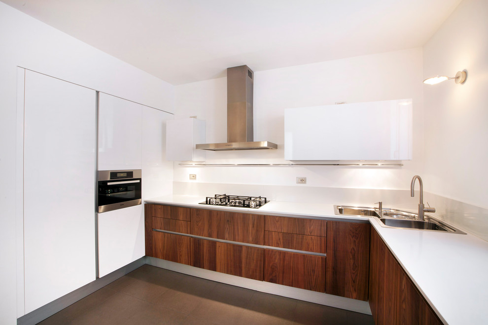 Стильный дизайн: угловая кухня в стиле модернизм с накладной мойкой, плоскими фасадами, темными деревянными фасадами, белым фартуком, техникой из нержавеющей стали и мойкой в углу - последний тренд