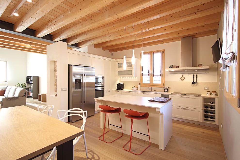 Modern inredning av ett kök, med en undermonterad diskho, skåp i shakerstil, vita skåp, beige stänkskydd, rostfria vitvaror, mellanmörkt trägolv och en köksö