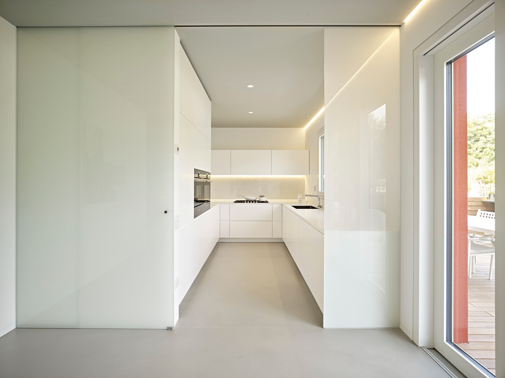 Cette image montre une cuisine design en U fermée avec un évier posé, des portes de placard blanches, un placard à porte plane et un électroménager en acier inoxydable.
