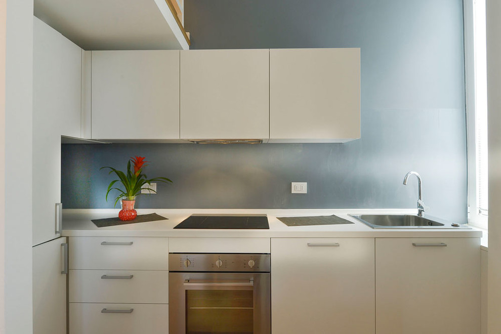 Foto på ett litet funkis vit kök, med en enkel diskho, släta luckor, vita skåp, laminatbänkskiva, blått stänkskydd, rostfria vitvaror och laminatgolv