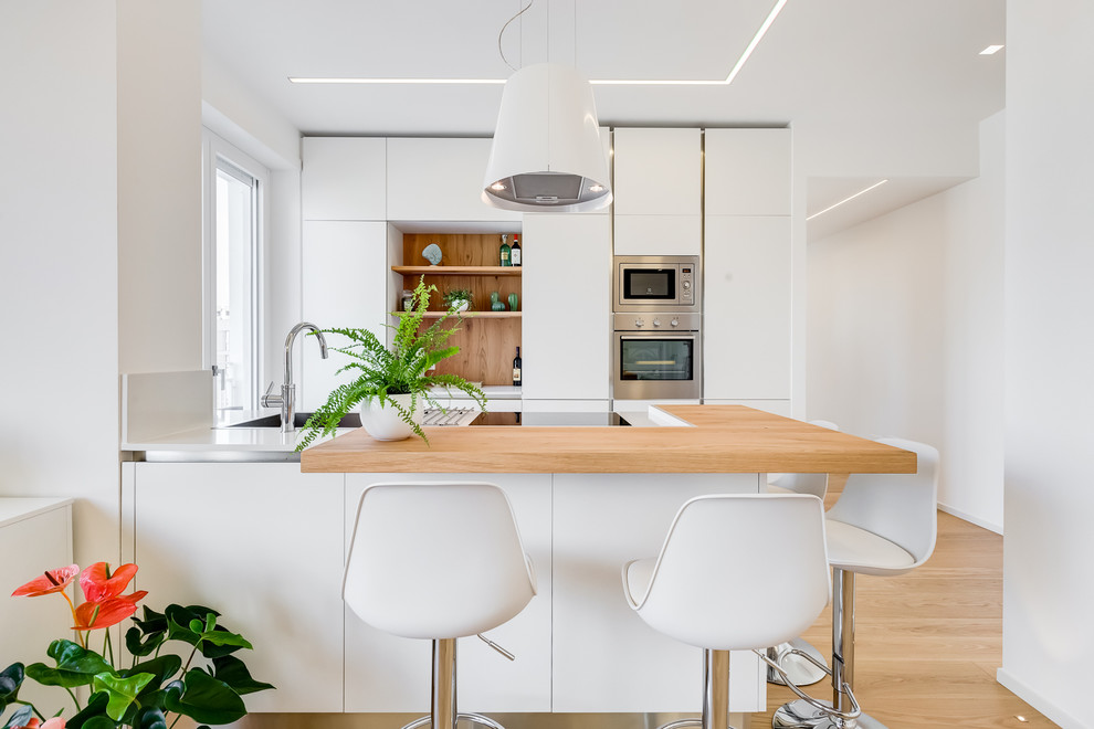 Design ideas for a contemporary galley kitchen in Rome with flat-panel cabinets, white cabinets, wood worktops, stainless steel appliances, light hardwood flooring, brown floors and brown worktops.