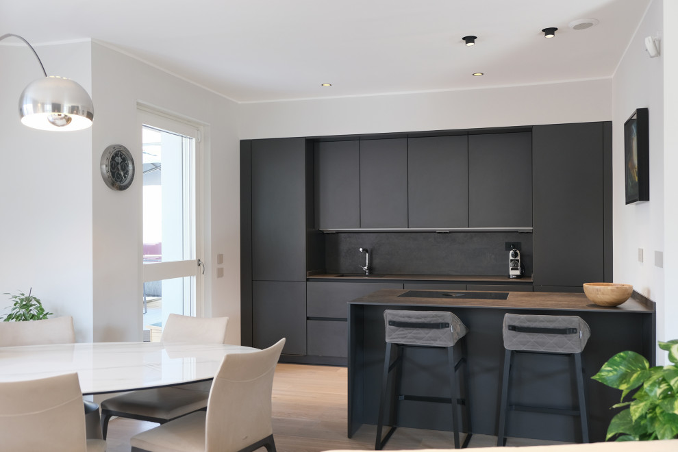 Cette image montre une cuisine parallèle et encastrable minimaliste avec un placard à porte plane, des portes de placard noires, une crédence noire, une péninsule, un sol marron et un plan de travail gris.