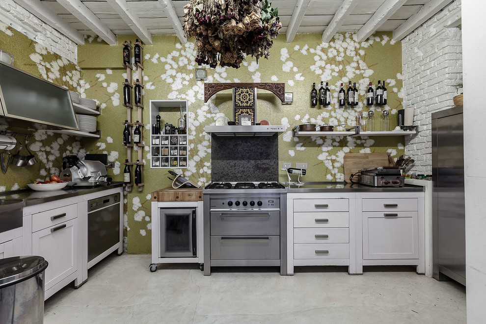 ミラノにある中くらいなエクレクティックスタイルのおしゃれなキッチン (インセット扉のキャビネット、白いキャビネット、ステンレスカウンター、シルバーの調理設備、コンクリートの床、壁紙) の写真