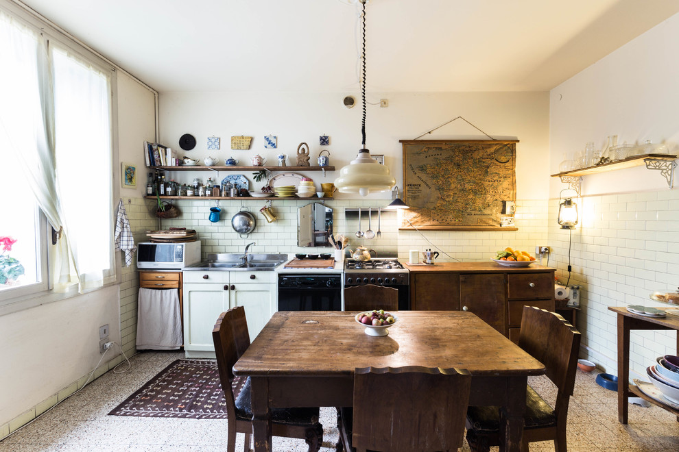 Photo of an eclectic single-wall kitchen/diner in Other with a double-bowl sink, flat-panel cabinets, dark wood cabinets, white splashback, metro tiled splashback, black appliances, no island and grey floors.