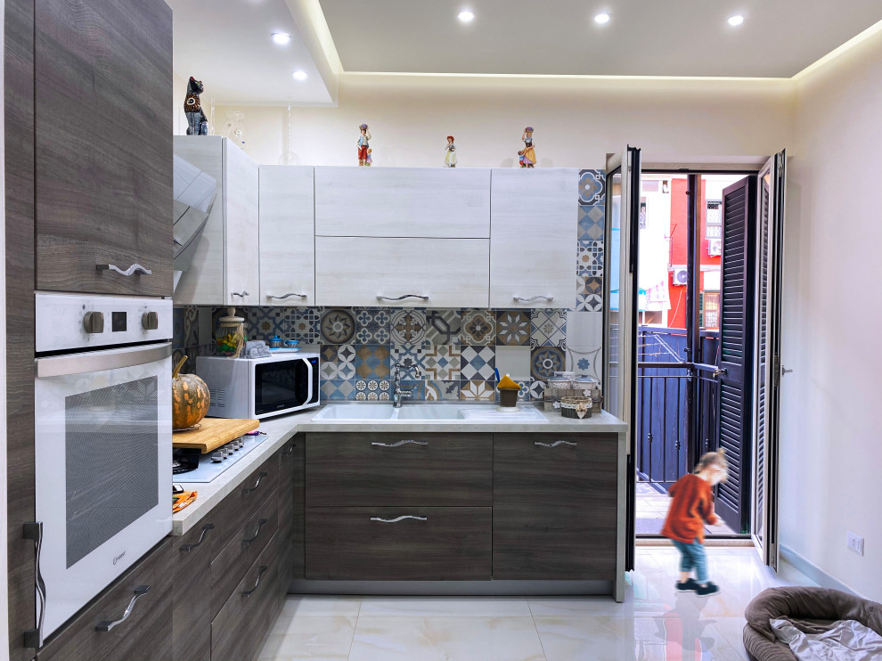 Small vintage l-shaped enclosed kitchen in Naples with a double-bowl sink, flat-panel cabinets, multi-coloured splashback, ceramic splashback, white appliances, ceramic flooring, no island, beige floors, white worktops and a coffered ceiling.