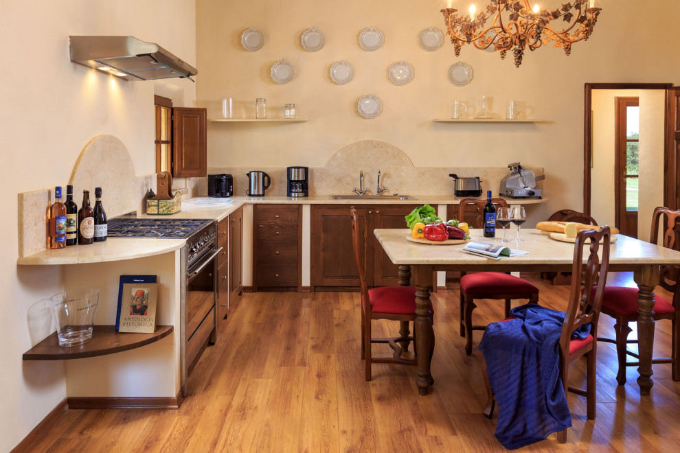 他の地域にある地中海スタイルのおしゃれなキッチン (シェーカースタイル扉のキャビネット、中間色木目調キャビネット、ベージュキッチンパネル、シルバーの調理設備、無垢フローリング、茶色い床、ベージュのキッチンカウンター) の写真
