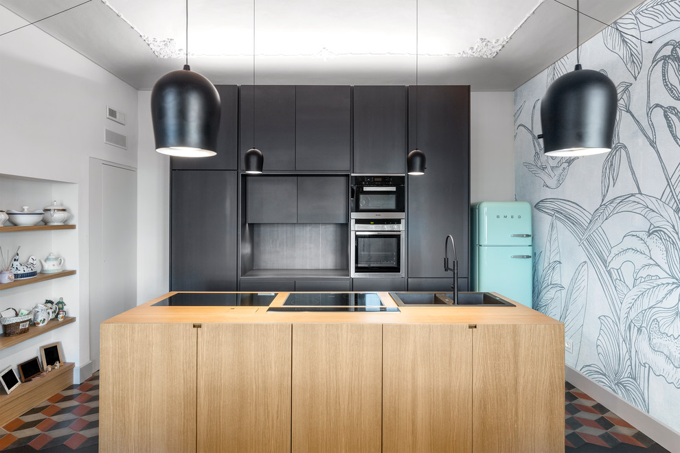 Inspiration for a contemporary galley kitchen/diner with a built-in sink, flat-panel cabinets, black cabinets, wood worktops, black splashback, coloured appliances, cement flooring, an island and multi-coloured floors.