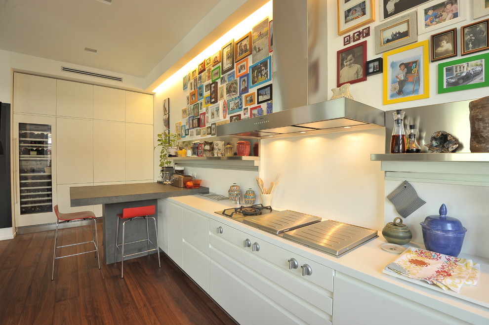 Cette image montre une grande cuisine ouverte linéaire design avec un placard à porte plane, des portes de placard blanches, un sol en bois brun, une crédence blanche et une péninsule.