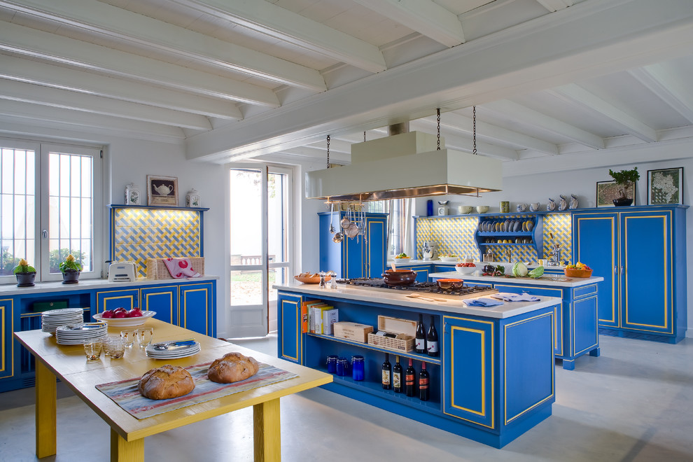 Modelo de cocina industrial extra grande con armarios con paneles empotrados, puertas de armario azules, salpicadero amarillo, dos o más islas y salpicadero de azulejos de cerámica