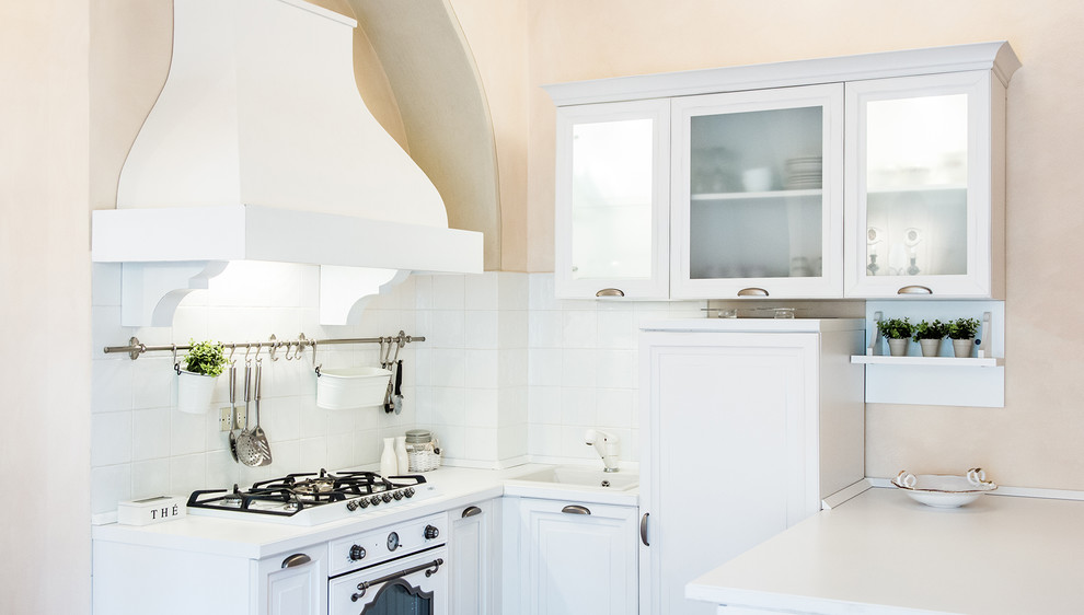 Esempio di una piccola cucina a L mediterranea con lavello da incasso, ante bianche, paraspruzzi bianco, elettrodomestici bianchi e penisola