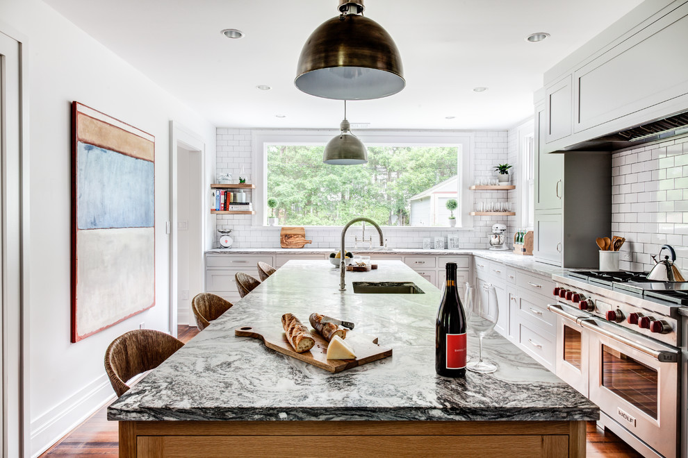 Example of a large classic l-shaped medium tone wood floor and brown floor eat-in kitchen design in Other with an undermount sink, shaker cabinets, white cabinets, marble countertops, white backsplash, subway tile backsplash, stainless steel appliances and an island