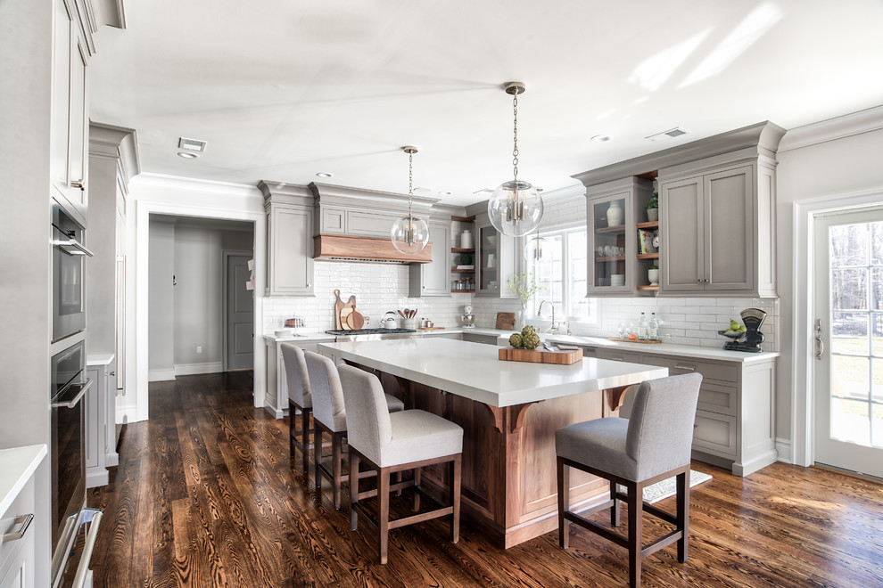 Elegant u-shaped dark wood floor and brown floor open concept kitchen photo in Other with a farmhouse sink, shaker cabinets, medium tone wood cabinets, concrete countertops, white backsplash, subway tile backsplash, black appliances, an island and gray countertops