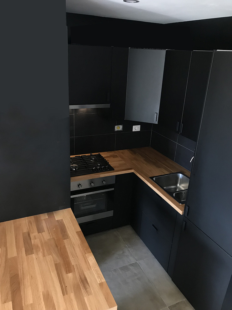 Пример оригинального дизайна: угловая кухня-гостиная в современном стиле с двойной мойкой, плоскими фасадами, черными фасадами, деревянной столешницей, техникой из нержавеющей стали, бетонным полом, островом и серым полом