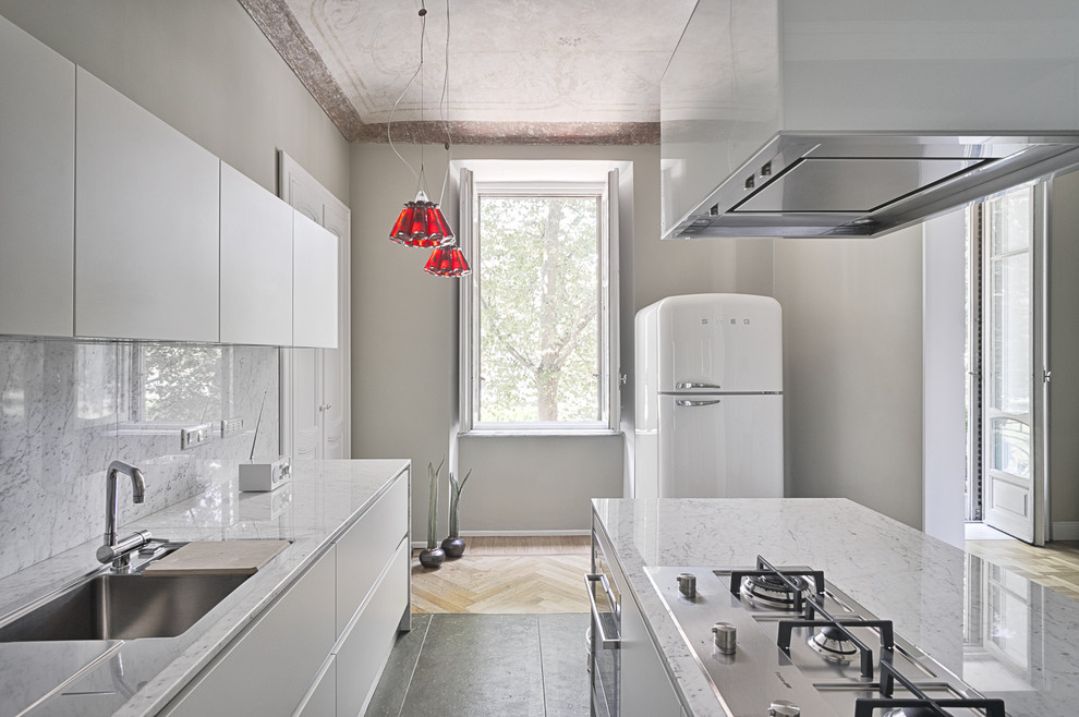 Bild på ett medelhavsstil u-kök, med vita skåp, en köksö, en undermonterad diskho, marmorbänkskiva, stänkskydd i sten och vita vitvaror