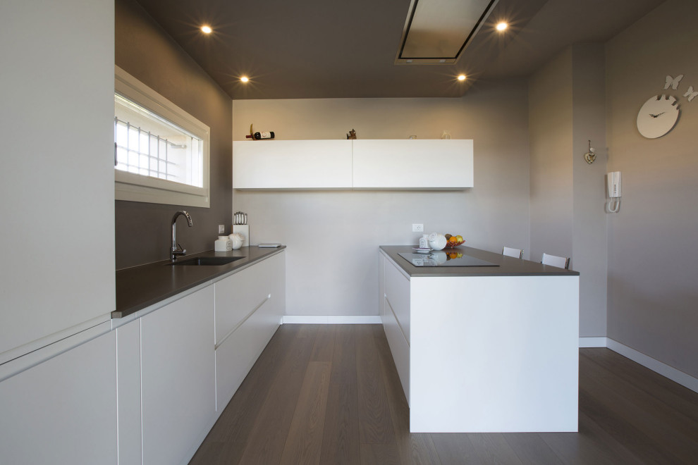 Esempio di una cucina parallela contemporanea di medie dimensioni con lavello integrato, ante lisce, ante bianche, penisola, pavimento marrone e top grigio
