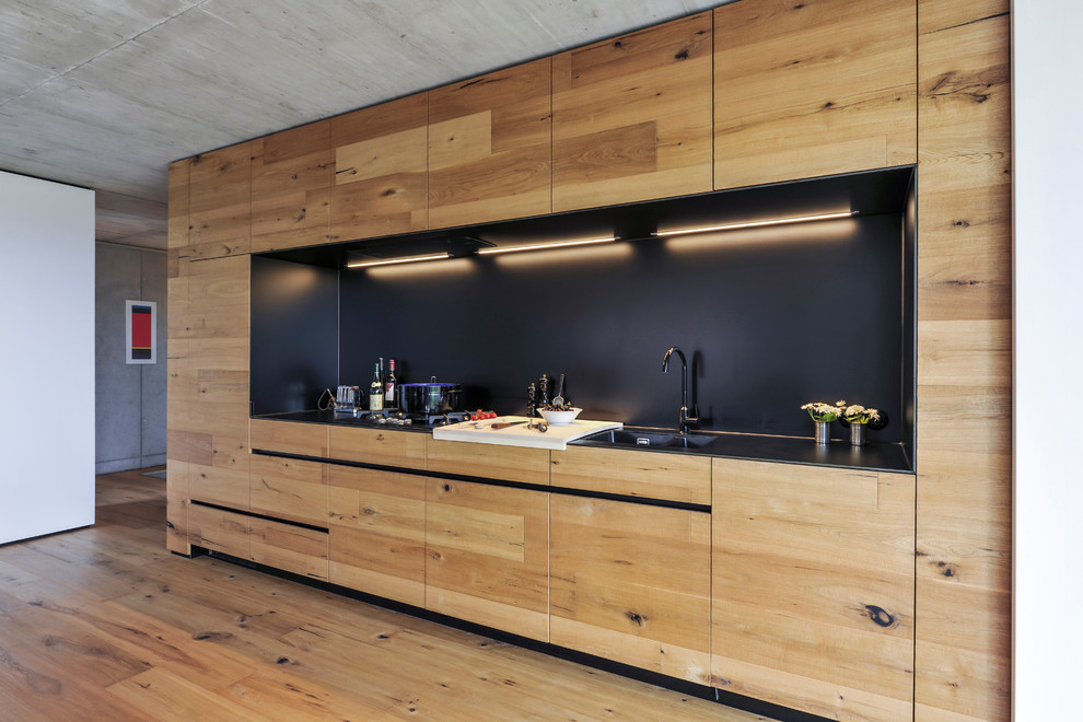 Foto di una cucina design di medie dimensioni con ante lisce, ante in legno chiaro, paraspruzzi nero, nessuna isola, lavello integrato, elettrodomestici da incasso e pavimento in legno massello medio