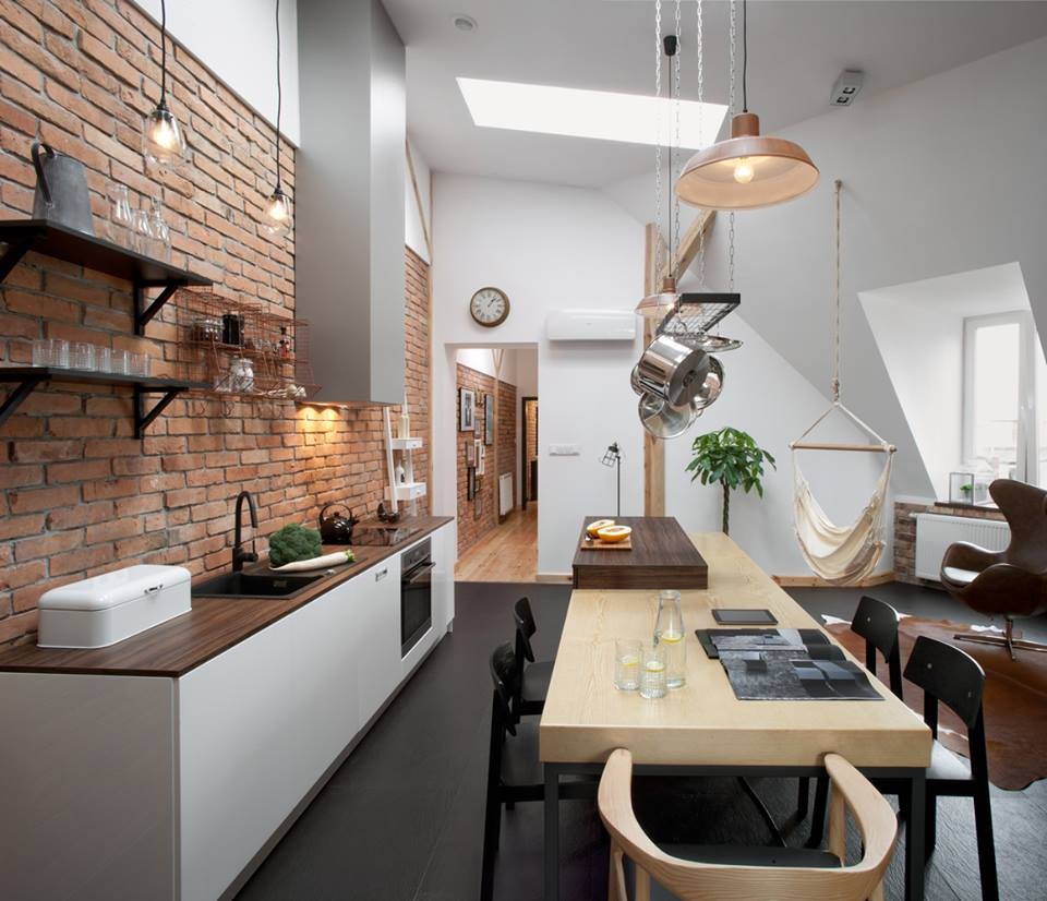 This is an example of a medium sized industrial single-wall open plan kitchen in Other with flat-panel cabinets, white cabinets, wood worktops, brown splashback, brick splashback, stainless steel appliances, an island and black floors.