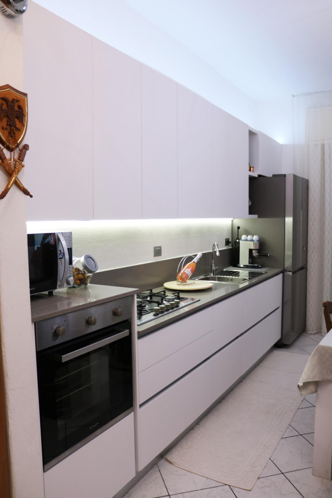 Inredning av ett modernt litet grå linjärt grått kök, med en nedsänkt diskho, vita skåp, bänkskiva i kvarts, grått stänkskydd, rostfria vitvaror och klinkergolv i keramik