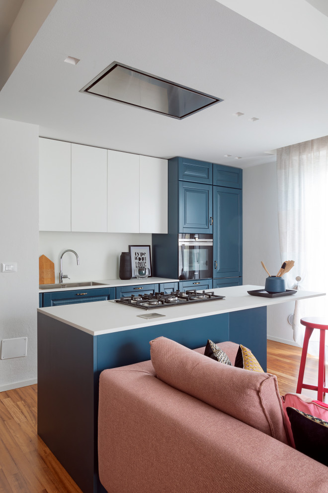 Inspiration for a medium sized contemporary galley open plan kitchen in Bologna with a built-in sink, flat-panel cabinets, blue cabinets, stainless steel appliances, medium hardwood flooring, an island, brown floors and white worktops.