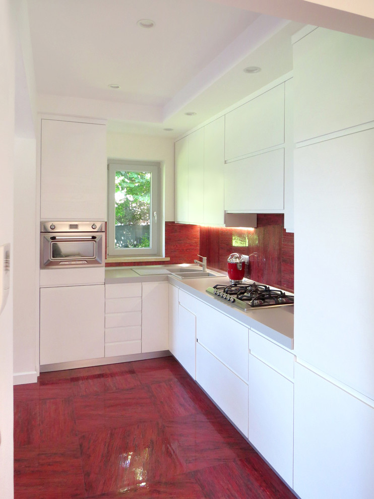 Moderne Küche ohne Insel in L-Form mit Doppelwaschbecken, flächenbündigen Schrankfronten, weißen Schränken, Küchenrückwand in Rot, Küchengeräten aus Edelstahl, grauer Arbeitsplatte und rotem Boden in Rom