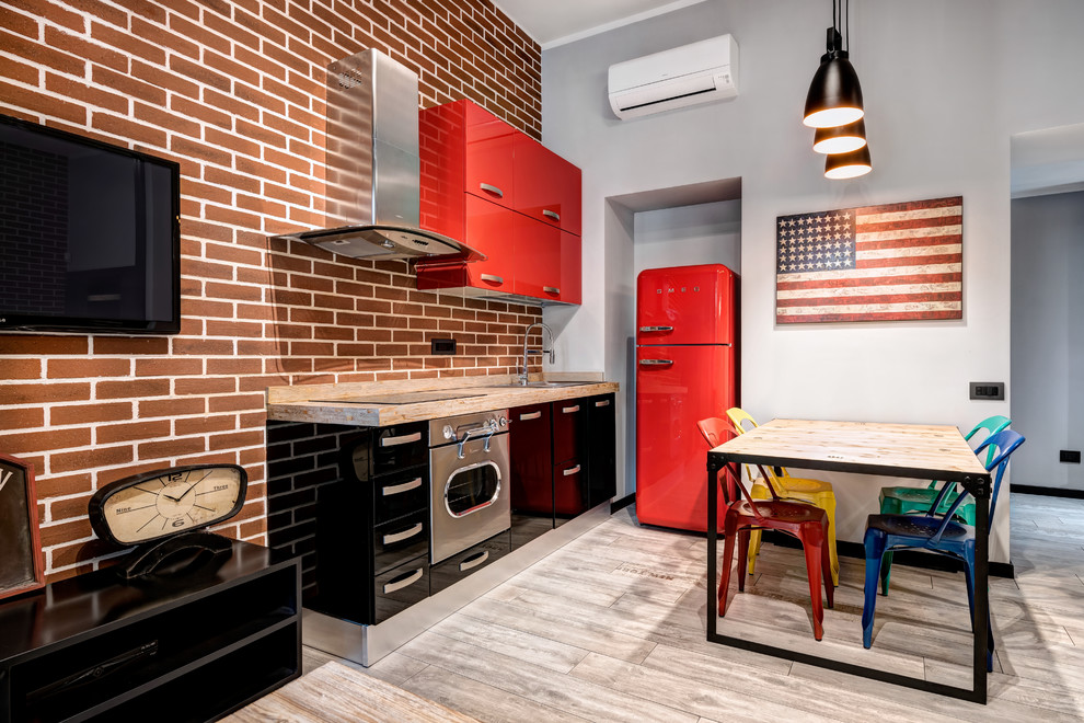 Cette photo montre une cuisine ouverte linéaire industrielle avec un plan de travail en bois, un sol en carrelage de porcelaine, un placard à porte plane, des portes de placard rouges, une crédence en brique, un électroménager de couleur et un sol beige.