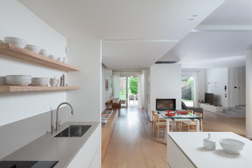 Foto di una cucina moderna chiusa e di medie dimensioni con lavello da incasso, paraspruzzi grigio, elettrodomestici neri, parquet chiaro e top grigio