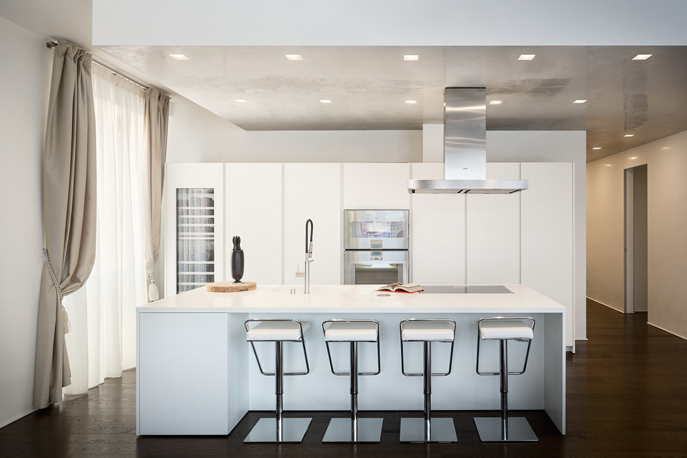 Large contemporary single-wall open plan kitchen in Milan with an integrated sink, flat-panel cabinets, white cabinets, dark hardwood flooring, an island and stainless steel appliances.