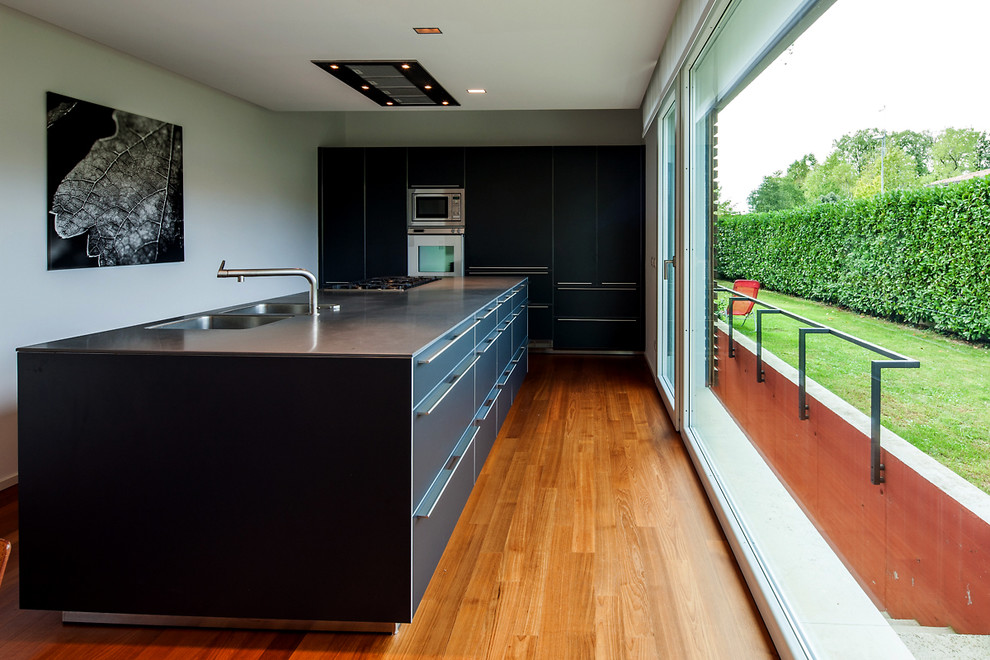 Einzeilige Moderne Küche mit flächenbündigen Schrankfronten, schwarzen Schränken, Edelstahl-Arbeitsplatte und Kücheninsel in Sonstige
