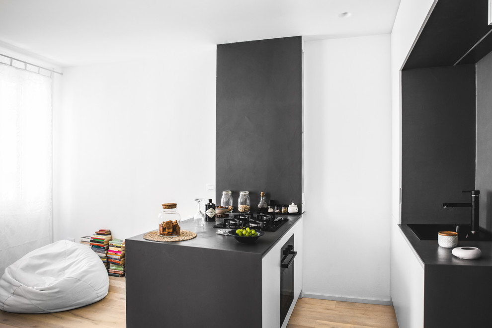 Imagen de cocina actual pequeña con fregadero encastrado, armarios con paneles lisos, puertas de armario blancas, salpicadero negro, suelo de madera clara y península
